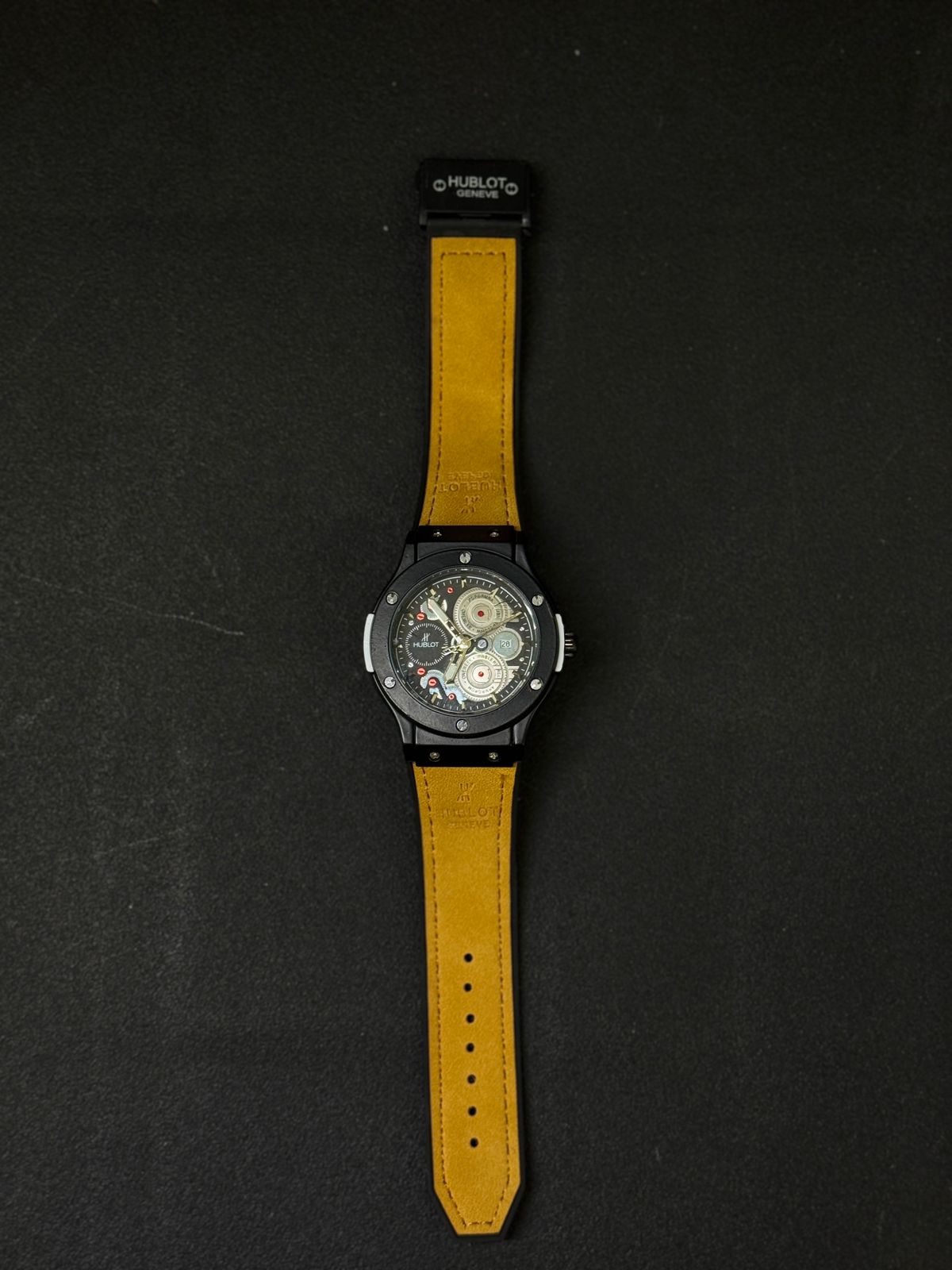 Full view of black replica watch with tan leather strap, skeleton gear dial, date display, luxury-inspired men's fashion watch on black surface