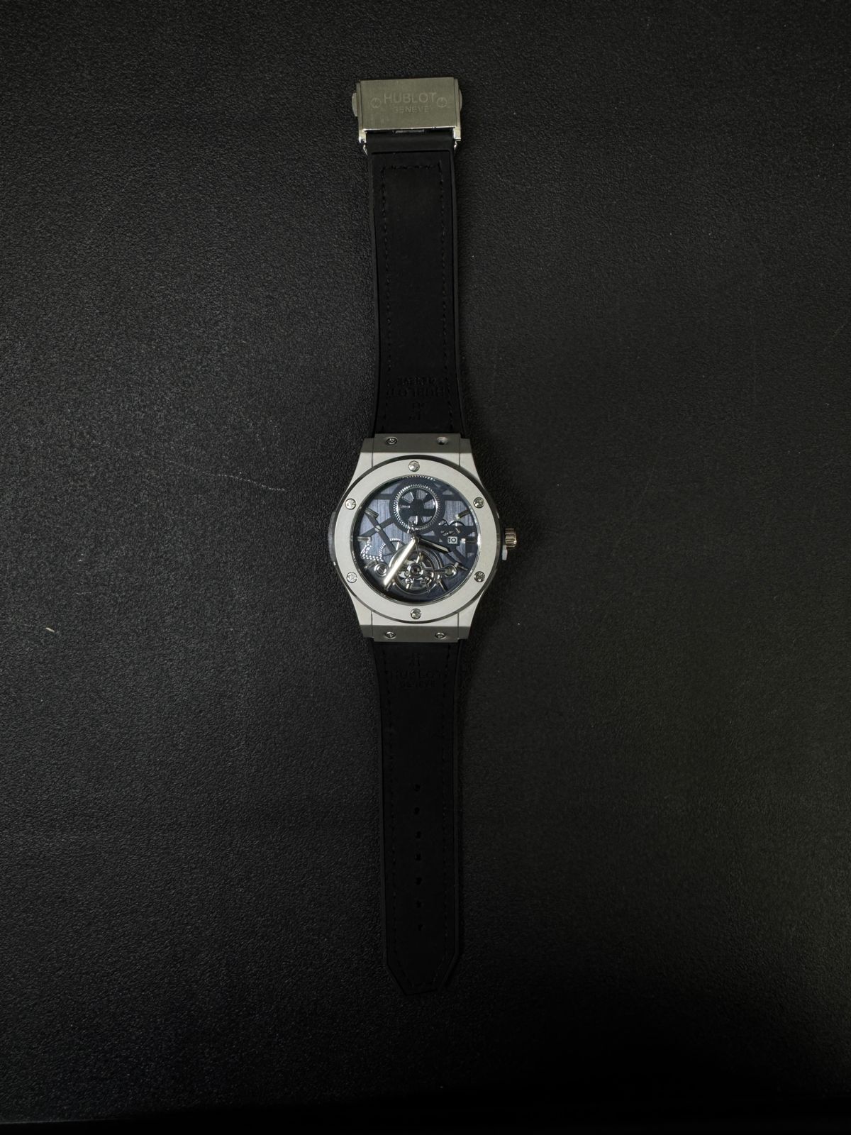 Hublot-inspired replica watch with silver case, blue open-work dial, black strap, and luxury skeleton movement design full view