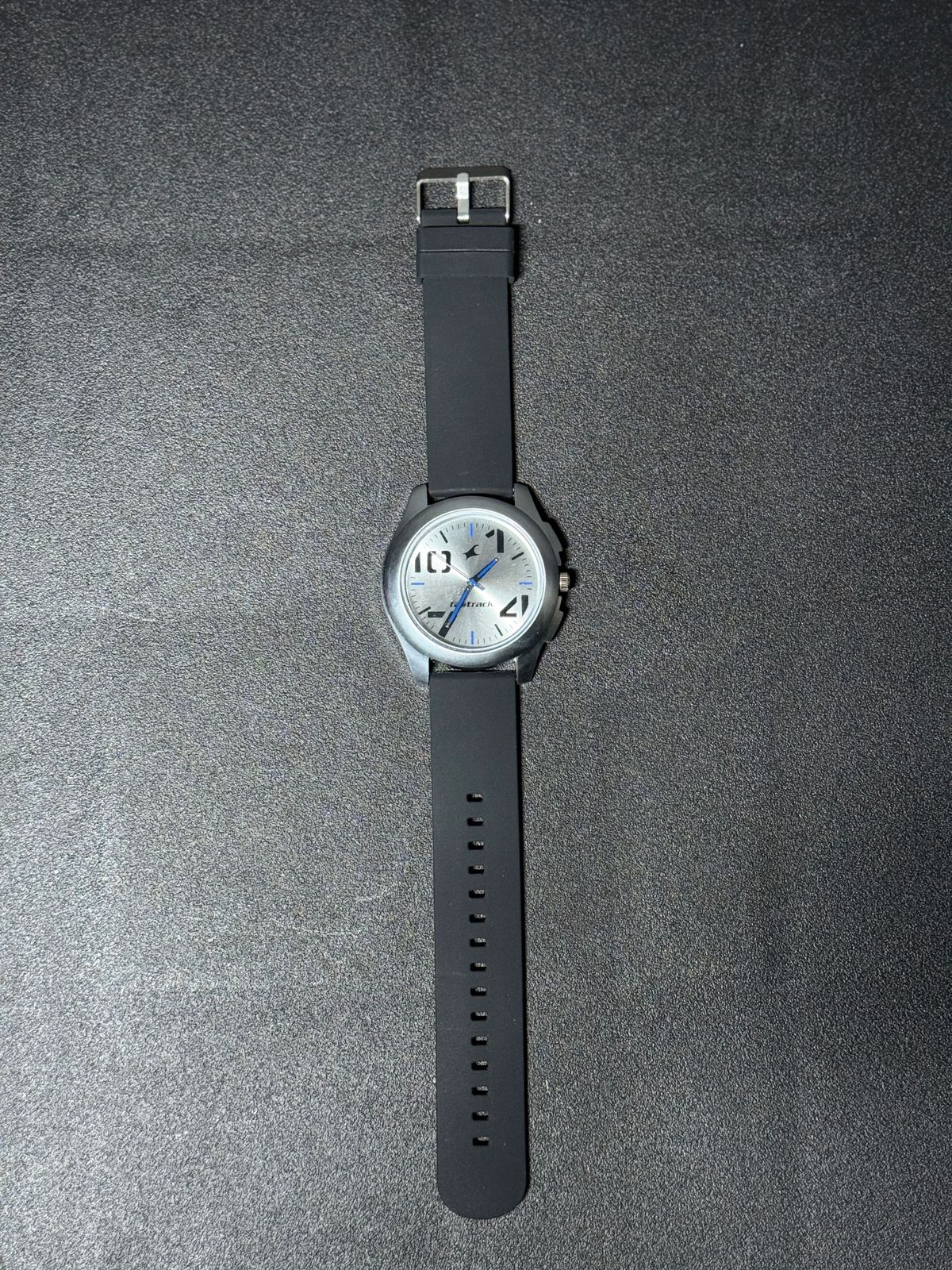 Replica Watch with black silicone strap, silver dial, blue accent hands and minimalist analog design, modern men's fashion wristwatch on black background.