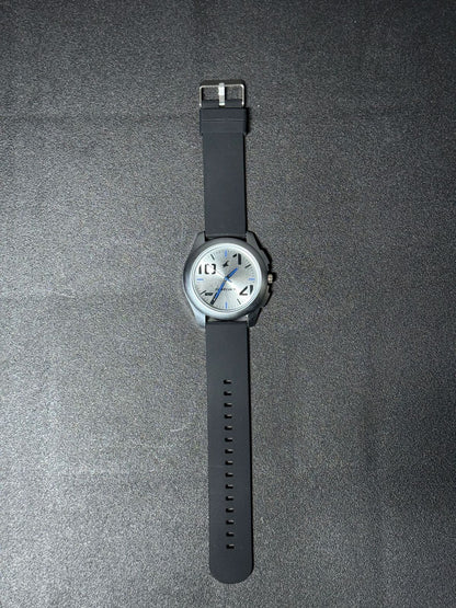 Replica Watch with black silicone strap, silver dial, blue accent hands and minimalist analog design, modern men's fashion wristwatch on black background.