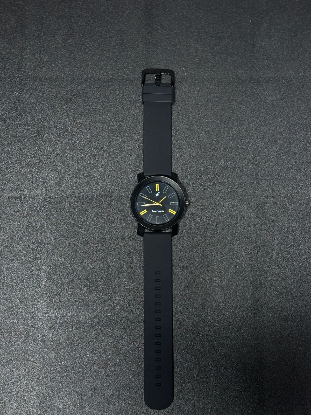 Replica watch with black silicone strap, black round dial, yellow accent markers and sleek minimalist analog design on dark background