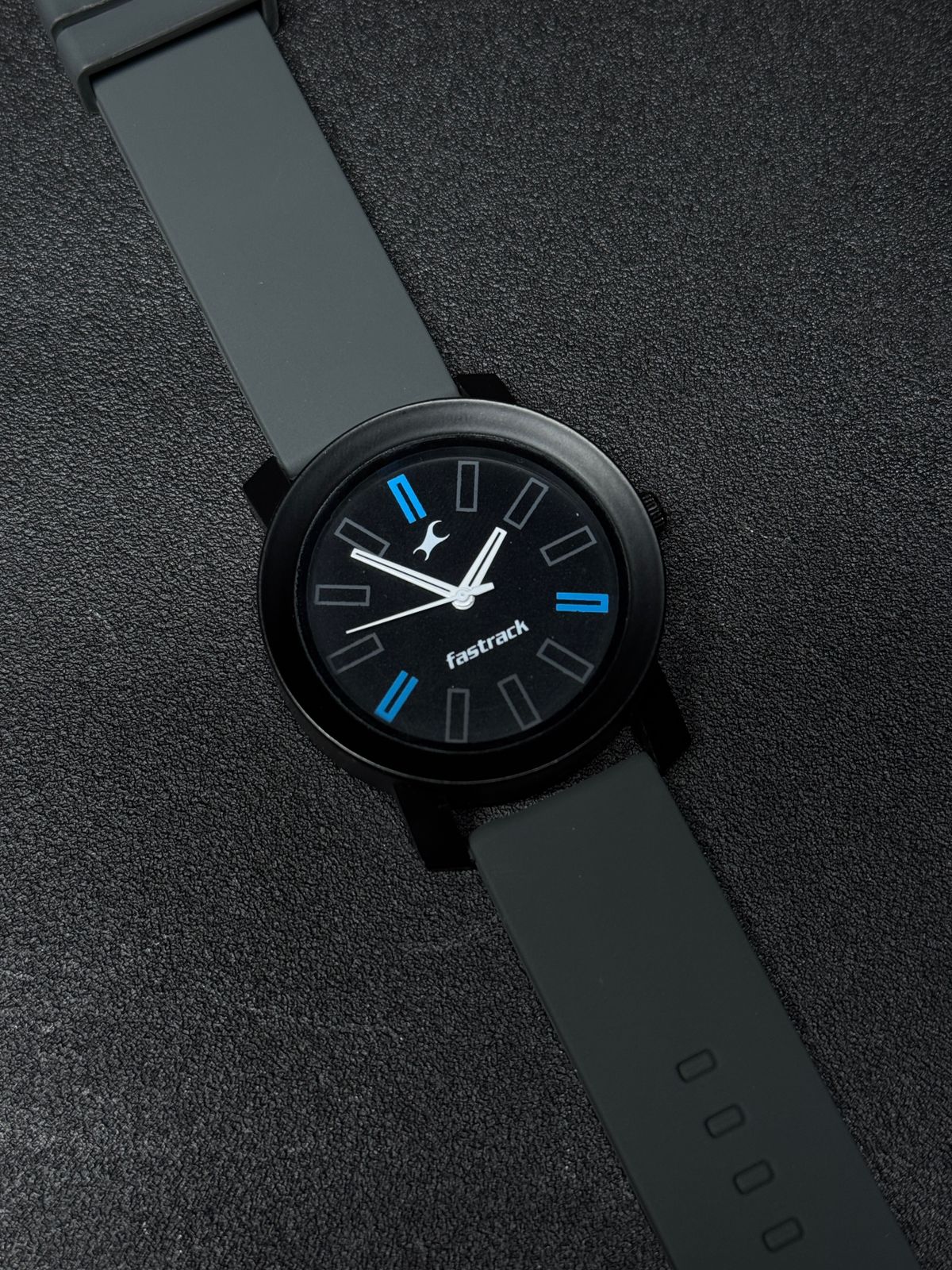 Close-up of replica analog watch featuring grey silicone strap, black dial with blue hour markers, matte black case and contemporary design