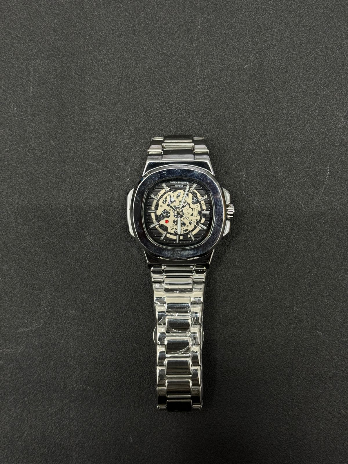 Replica watch with black skeleton dial and stainless steel bracelet, premium luxury-inspired men's wristwatch on dark background