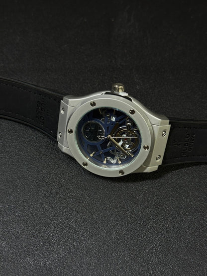 Luxury replica watch with blue skeleton dial, silver-tone case, black strap, and tourbillon-style open-heart display on dark background