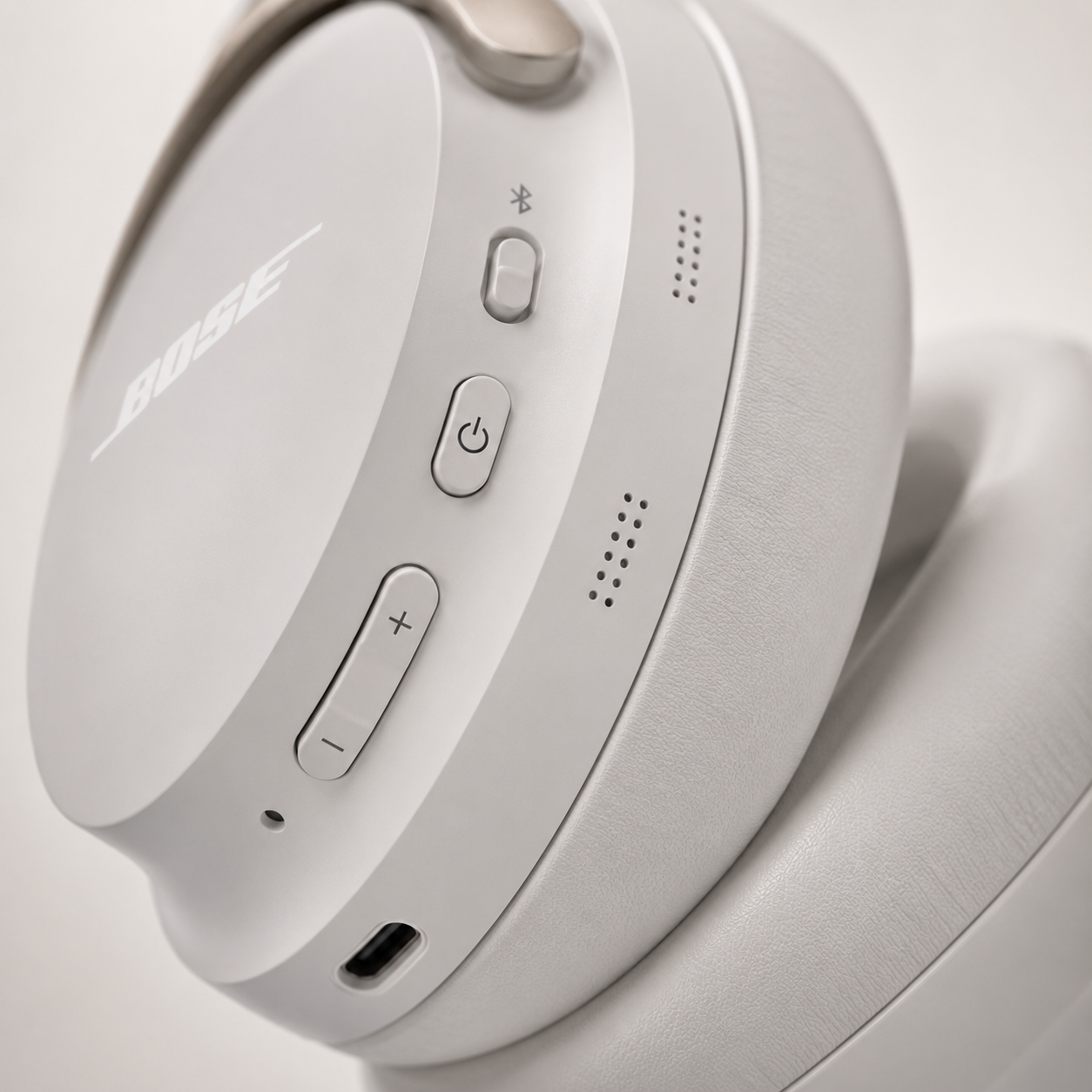 Close-up of white wireless Bluetooth over-ear headphones featuring power button, Bluetooth pairing button, volume controls, USB-C charging port and integrated microphones with premium matte finish.