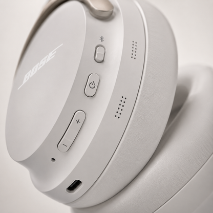 Close-up of white wireless Bluetooth over-ear headphones featuring power button, Bluetooth pairing button, volume controls, USB-C charging port and integrated microphones with premium matte finish.