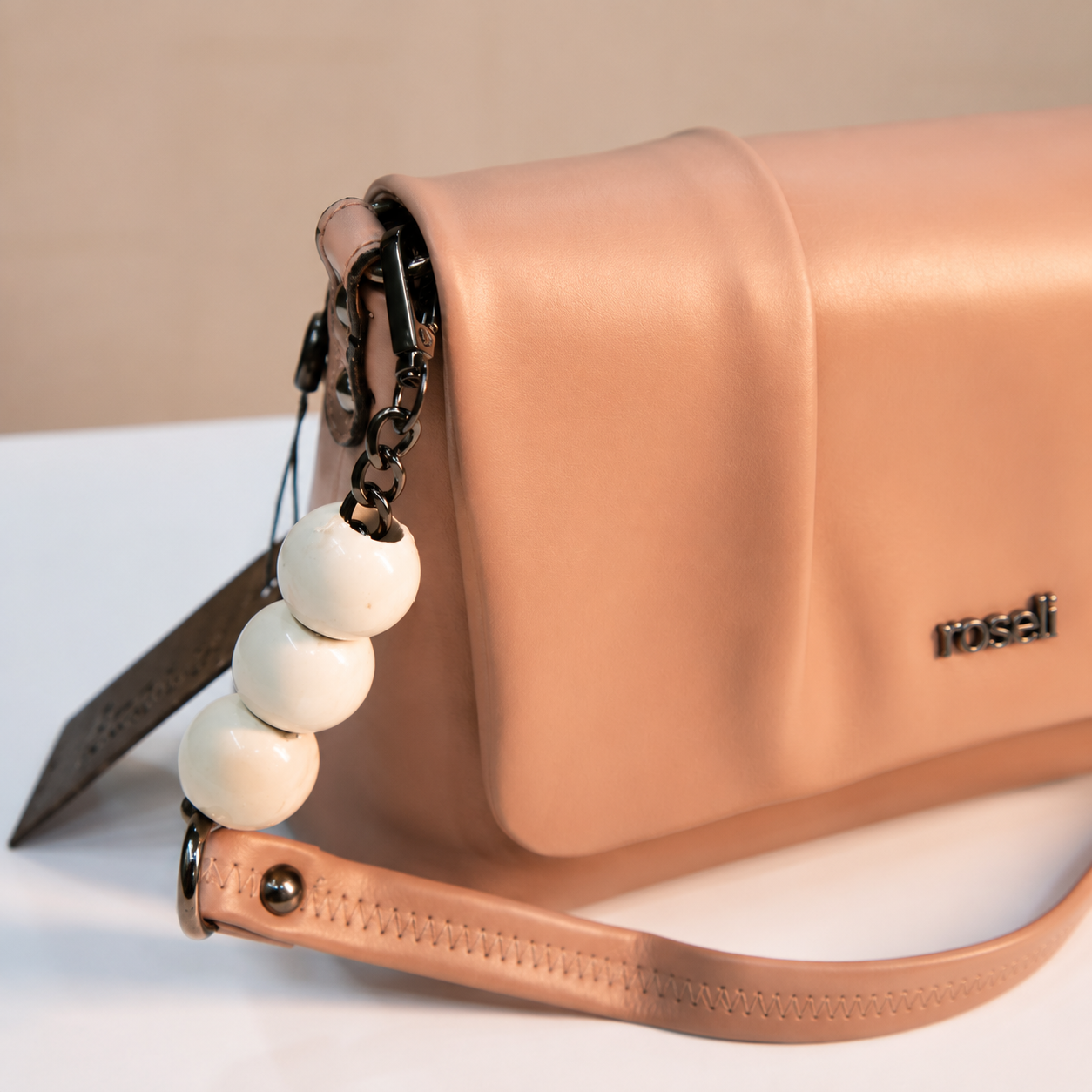 Close-up of a nude beige women's handbag highlighting the pleated flap, white beaded chain detail, dark metal hardware, and premium leather-look material.