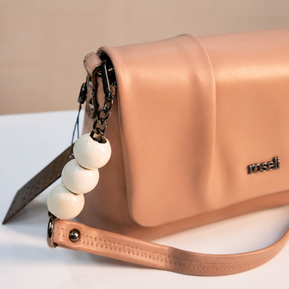 Close-up of a nude beige women's handbag highlighting the pleated flap, white beaded chain detail, dark metal hardware, and premium leather-look material.