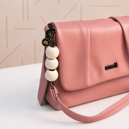 Close-up of a blush pink women's handbag showcasing the pleated flap design, decorative white beaded chain detail, dark metal hardware, and premium leather-look finish.