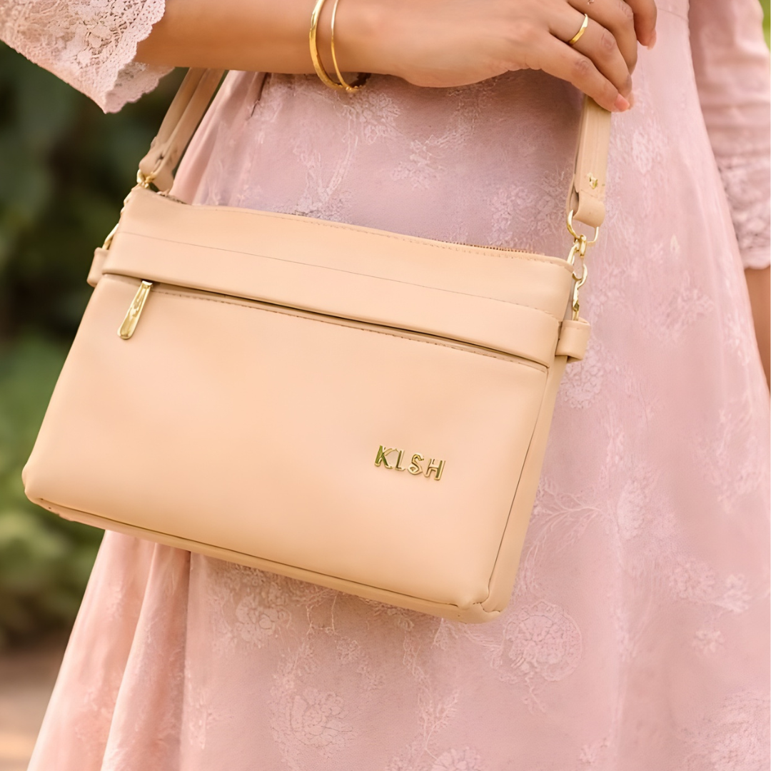 Beige crossbody sling bag with zip closure worn with casual outfit.